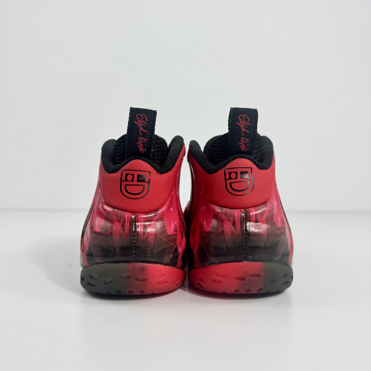 Nike Air Foamposite trainers in red and black with smiley faces on the heels, black pull tabs, and circular patterned soles.