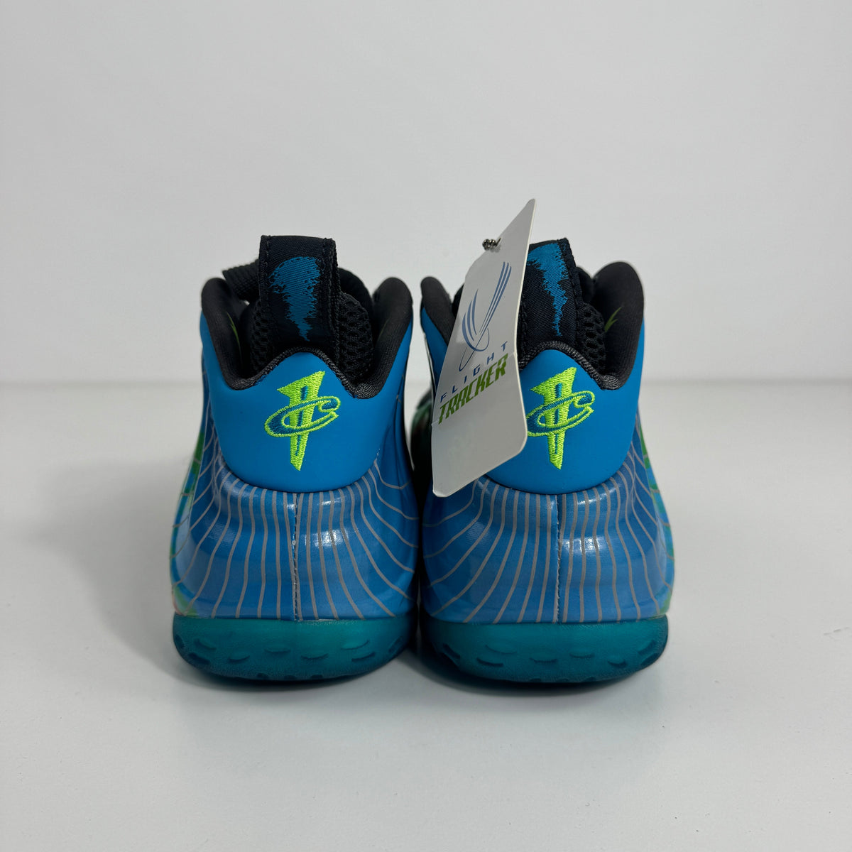 Nike Air Foamposite One trainers in blue with neon green logos, wavy white detailing and a branded tag, shown from the back.