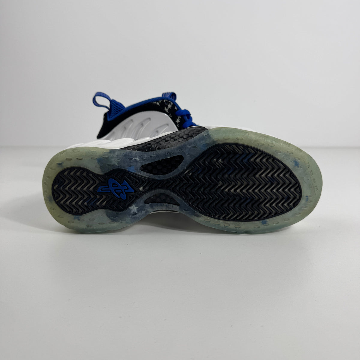 Close-up of a Nike trainer outsole with a translucent base, black herringbone grip, and blue details on a plain white background.