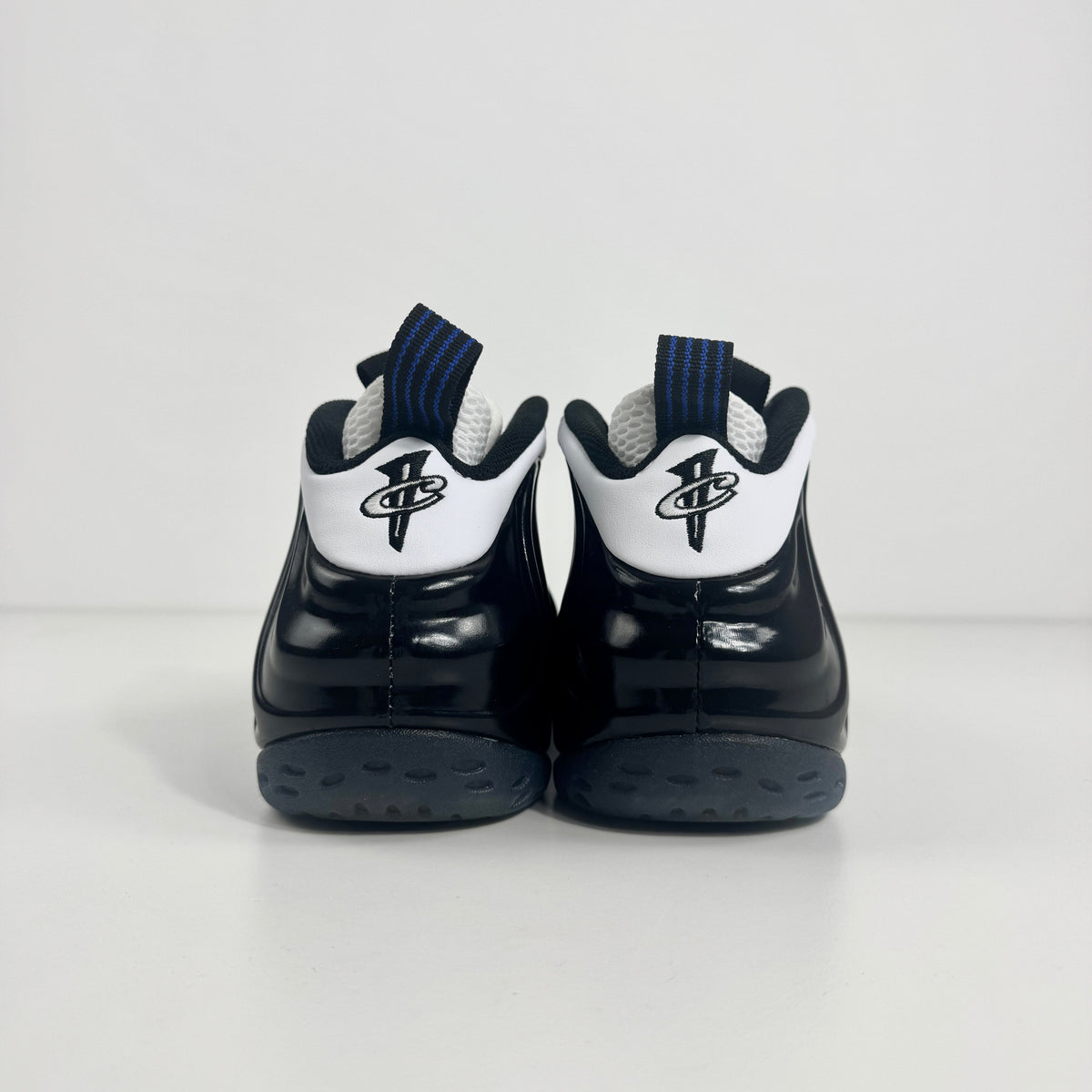 The Nike Air Foamposite One Concord UK 7 features a shiny black molded upper paired with stark white leather trim along the
