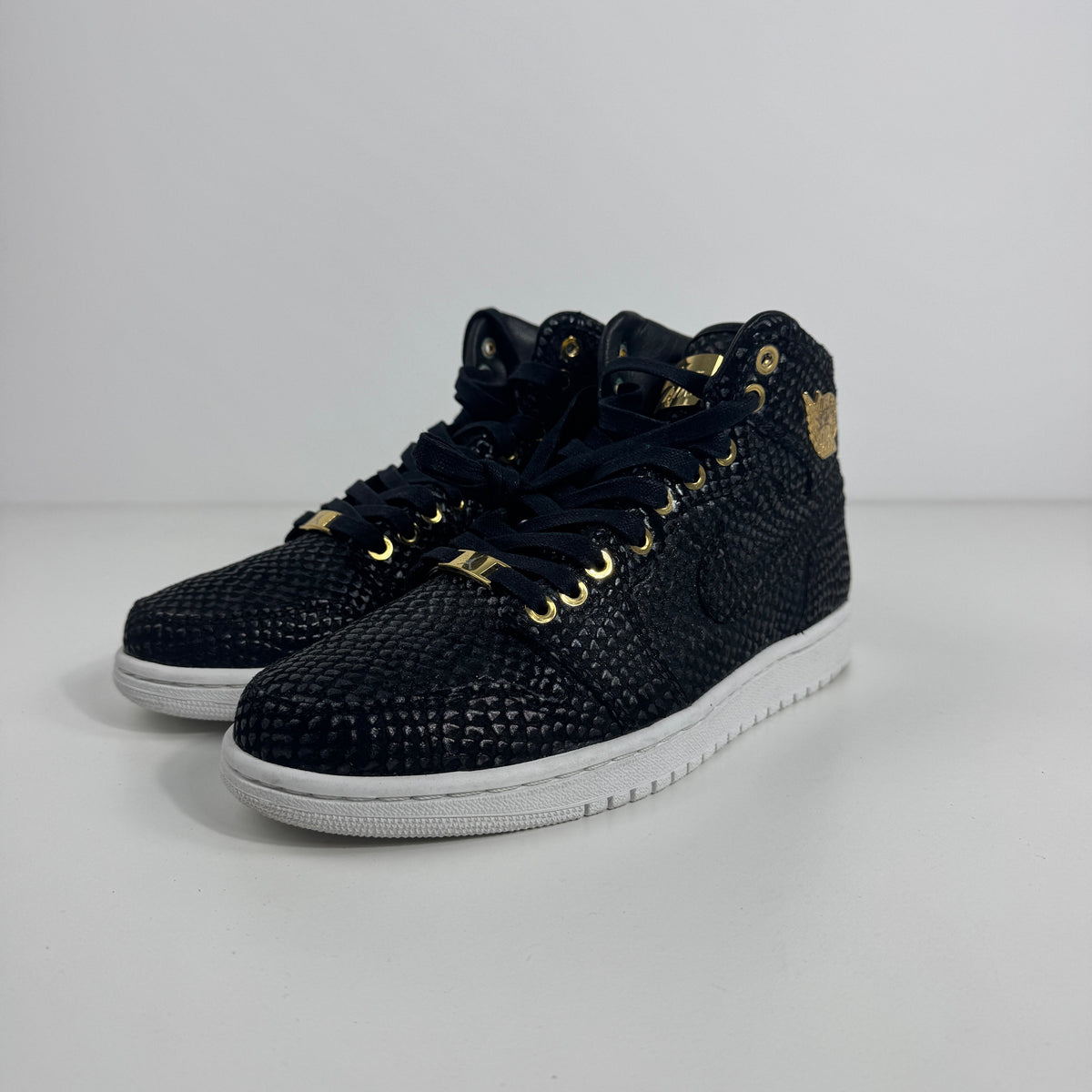 Nike Air Jordan 1 Pinnacle trainers in black textured material with gold accents, black laces and white soles on a white background.