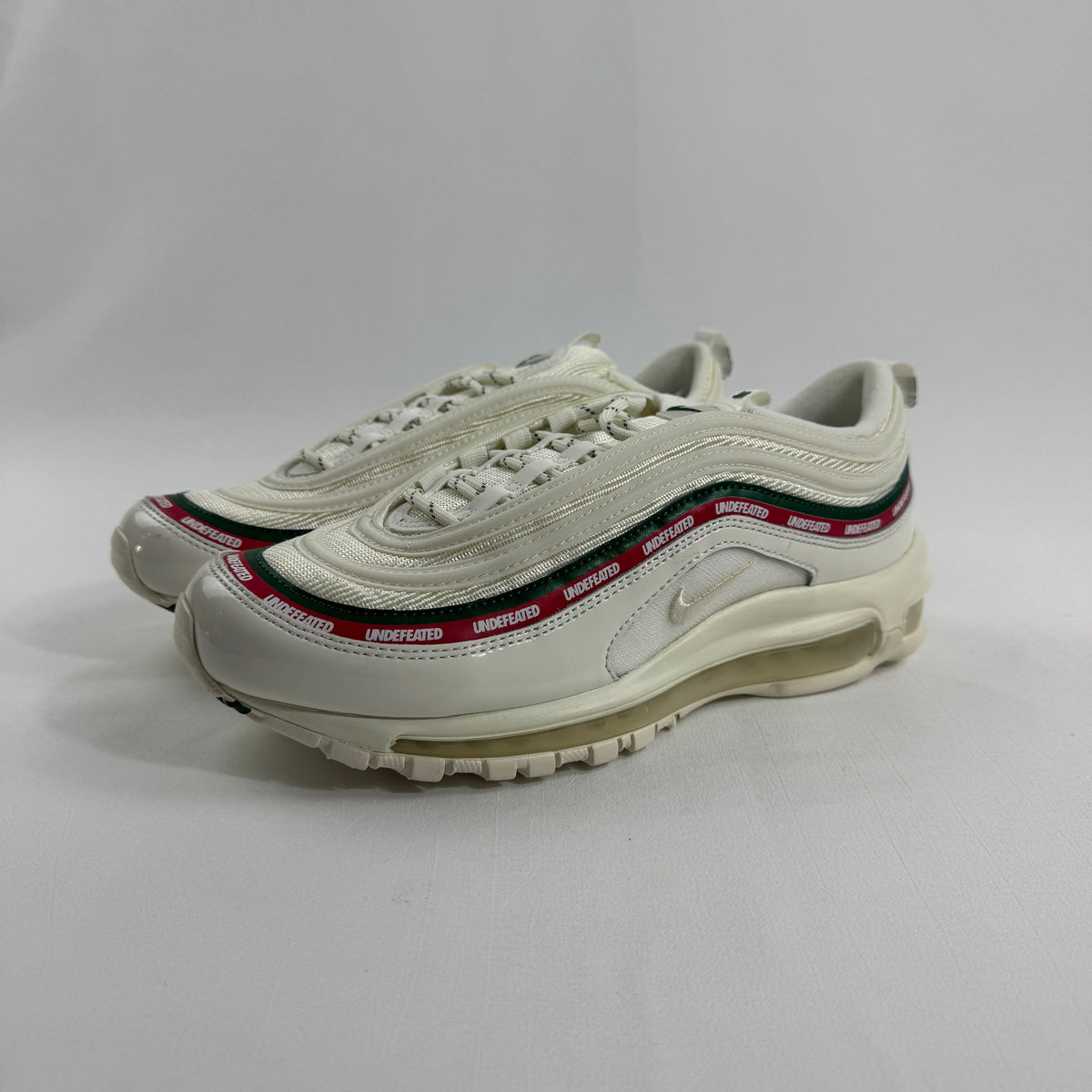 NIKE Air Max 97 Undefeated Sail trainers with cream soles and red, black and green accents on a plain white background.