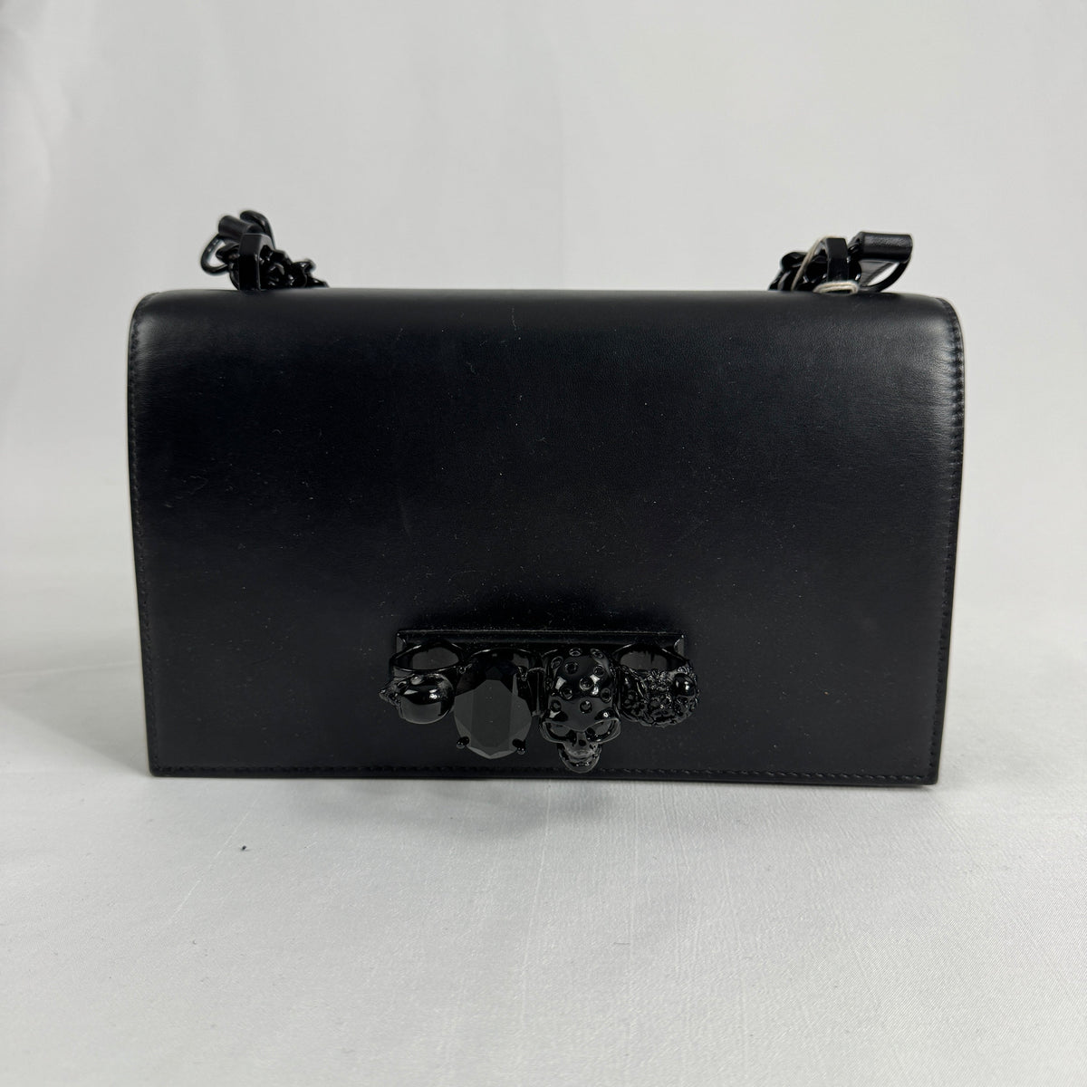 The Alexander McQueen Blackout Leather Crossbody Knuckle Bag is a bold statement piece featuring smooth black leather, a
