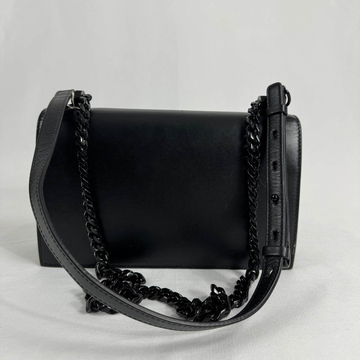 The Alexander McQueen Blackout Leather Crossbody Knuckle Bag is a bold statement piece featuring smooth black leather, a