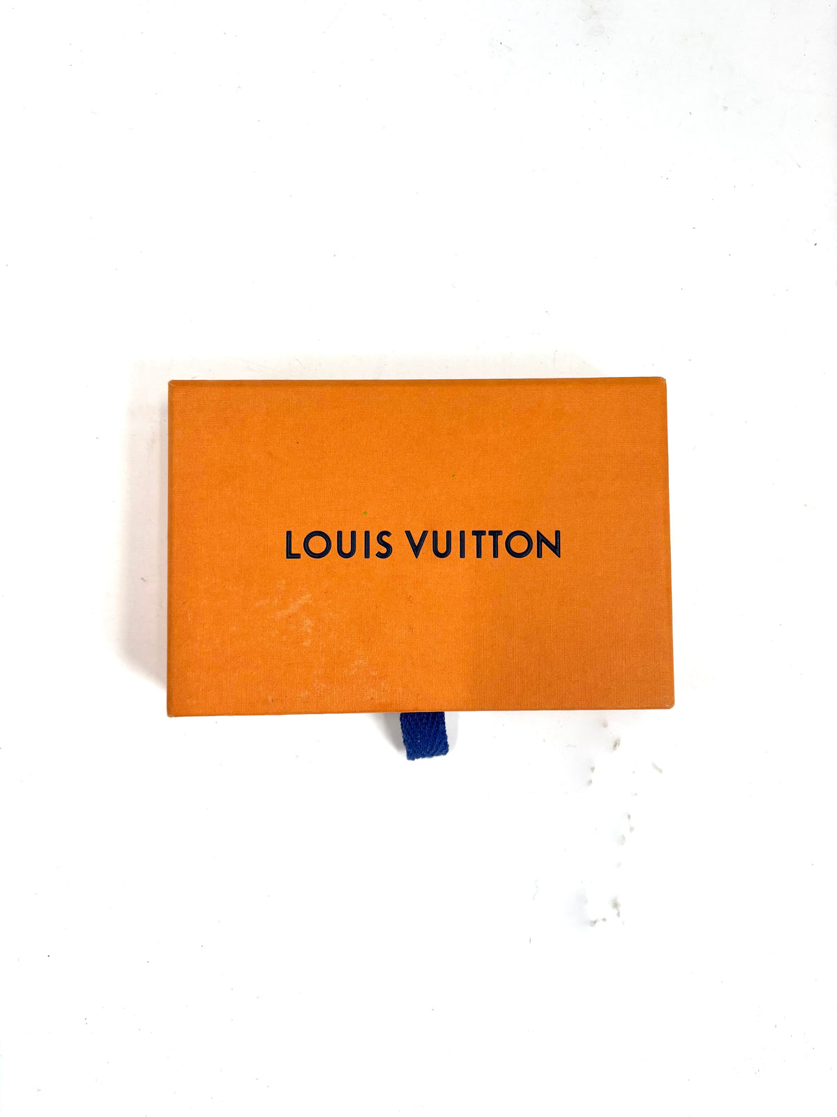 Orange Louis Vuitton box with black lettering and a blue pull tab, placed on a white surface.