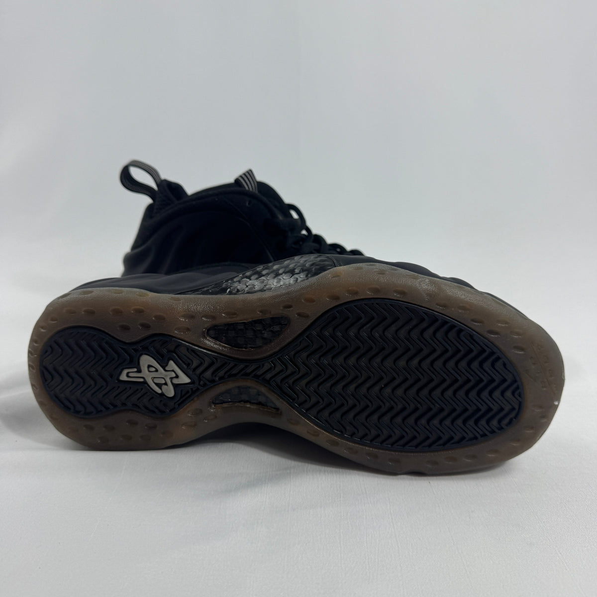 Black Nike basketball trainer on its side, showing a wavy textured sole and small white logo by the heel on a plain white background.