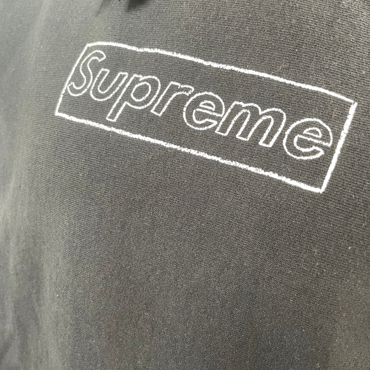 The Supreme KAWS Chalk Hooded Sweatshirt Black is a heavyweight cotton hoodie featuring KAWS’ signature chalk-style Box Logo